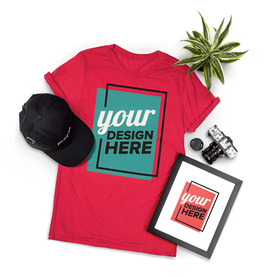 Red t-shirt, black baseball cap, picture frame says "your design here" laying on a white background next to a camera and plant