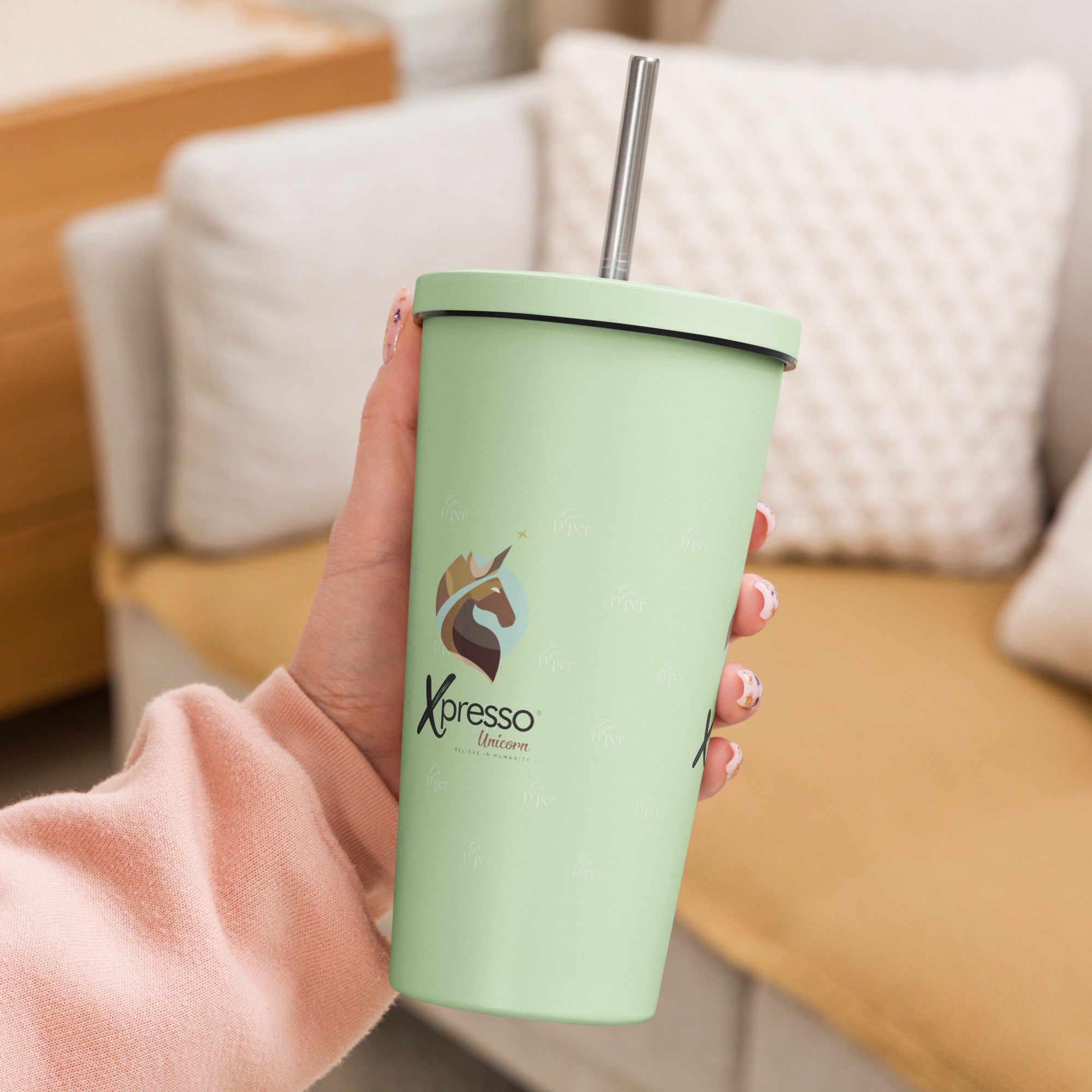 Close-up: A hand grips a mint green insulated tumbler with a straw. The Xpresso Unicorn logo is visible on the cup.