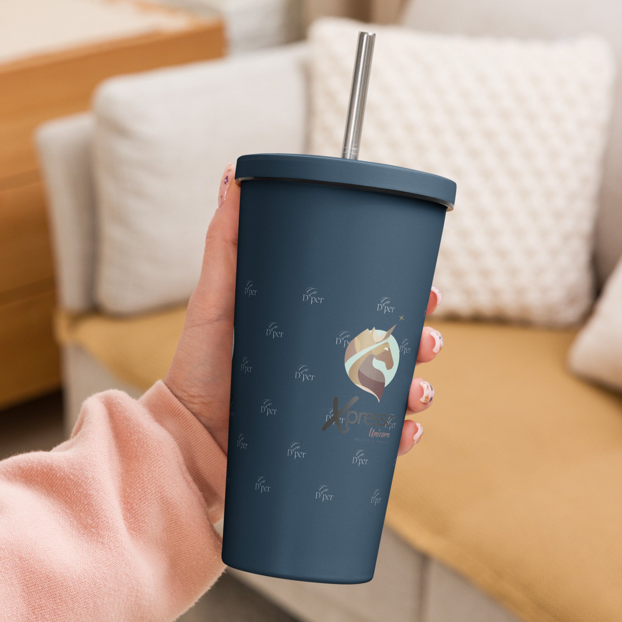 Close-up: A hand grips a navy blue insulated tumbler with a straw. The Xpresso Unicorn logo is subtly visible on the cup.