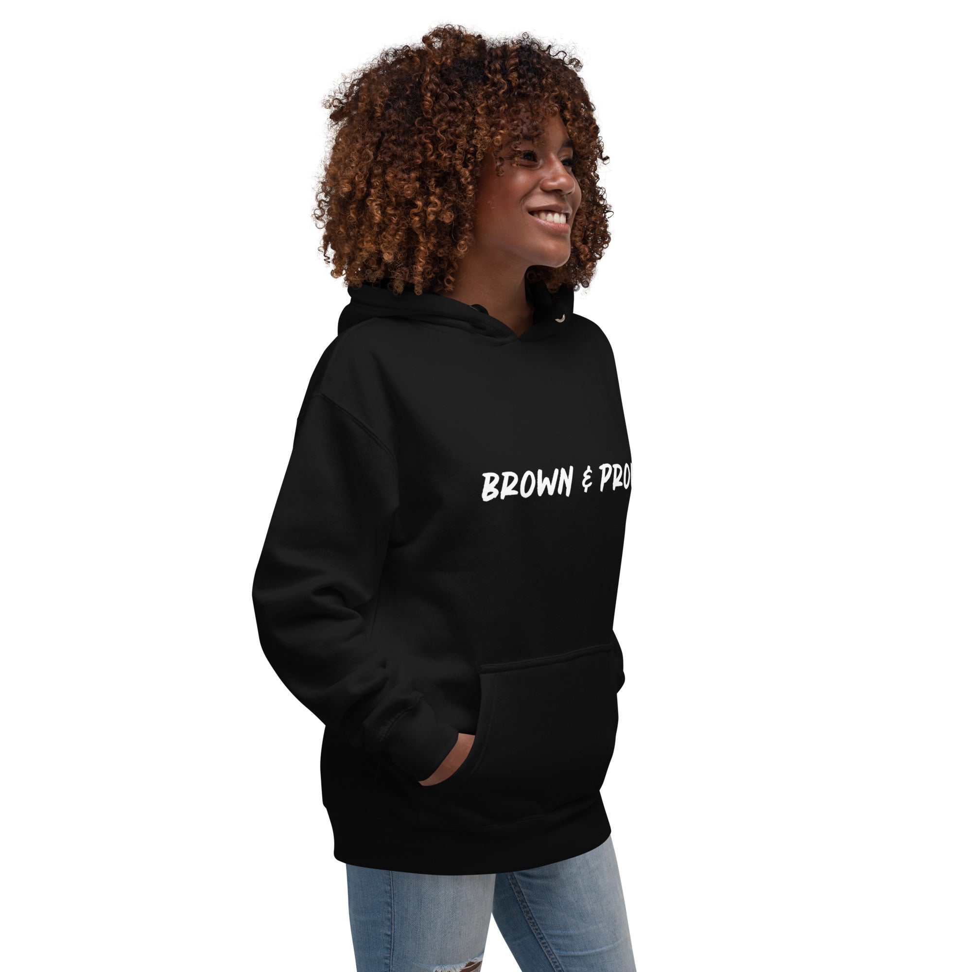 A radiant smile shines on a Black woman's face as she wears a navy blue hoodie proclaiming "Brown & Proud," capturing a moment of self-love and acceptance.