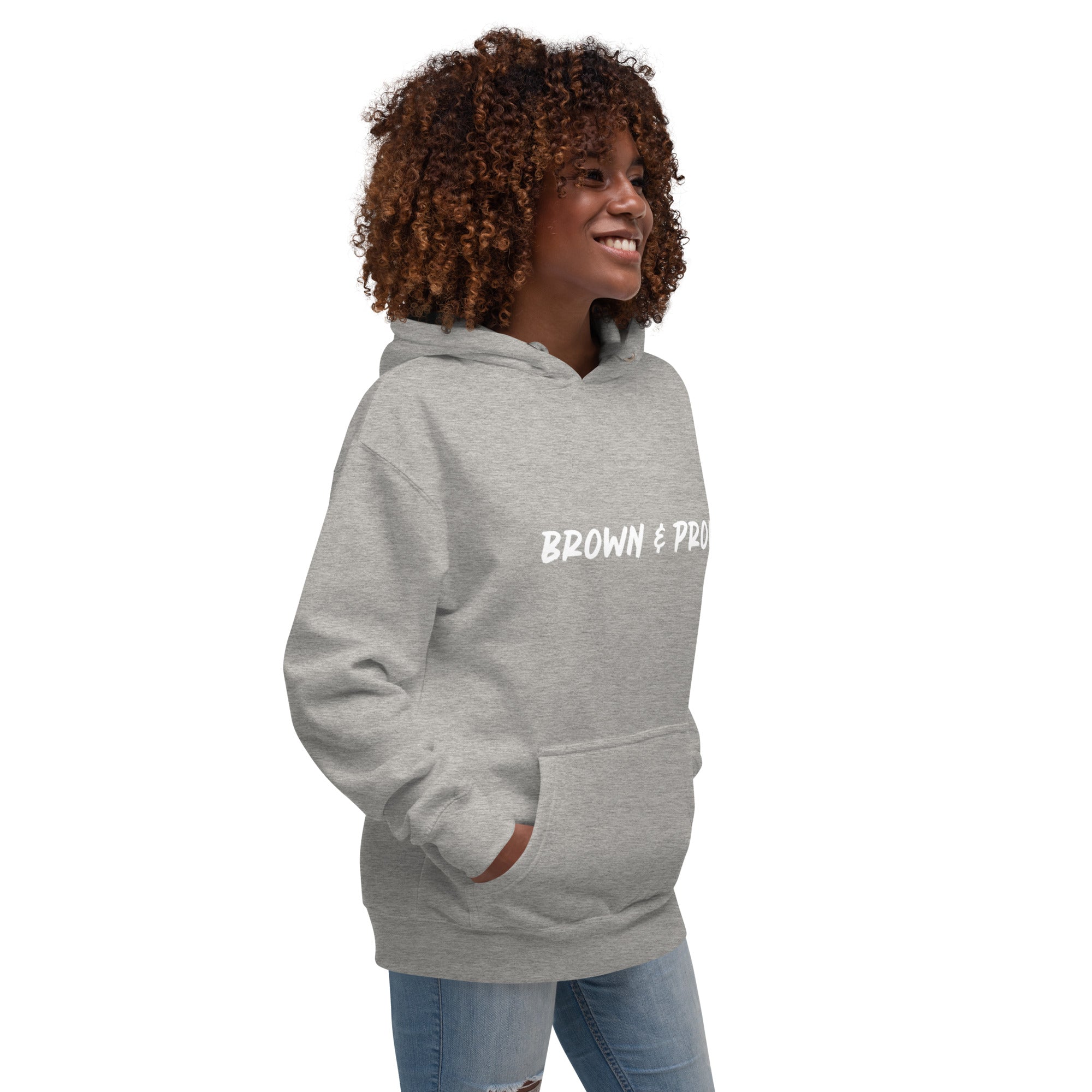 A Black woman radiates confidence, wearing a gray hoodie with the empowering message "Brown & Proud."