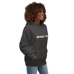 A person of color proudly wears a royal blue hoodie featuring the words "Brown & Proud," celebrating their heritage.