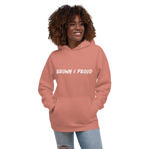 A Black woman smiles, sporting a dusty rose hoodie with the words "Brown & Proud" printed boldly across the chest.