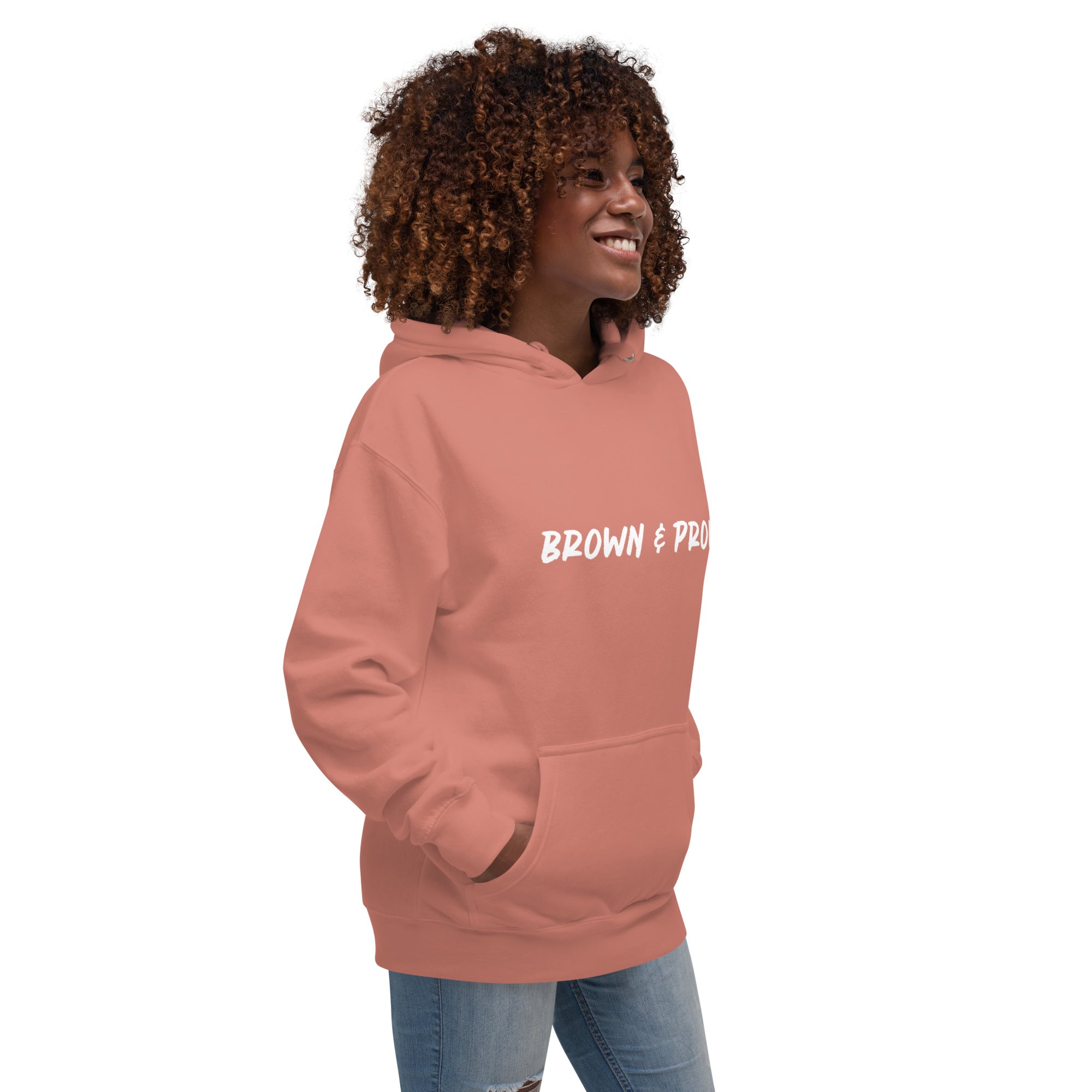 A Black woman radiates confidence, wearing a dusty rose hoodie with the empowering message "Brown & Proud."