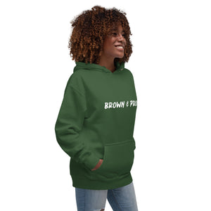 A radiant smile shines on a Black woman's face as she wears a military green hoodie proclaiming "Brown & Proud," capturing a moment of self-love and acceptance.