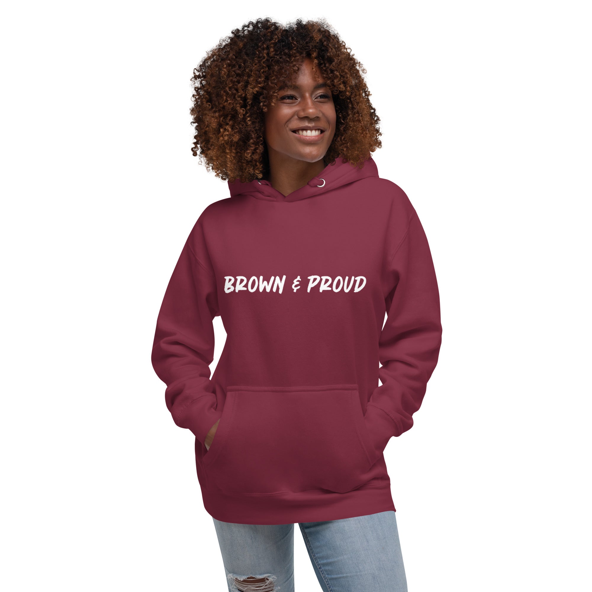 A radiant smile shines on a Black woman's face as she wears a maroon hoodie proclaiming "Brown & Proud," capturing a moment of self-love and acceptance.