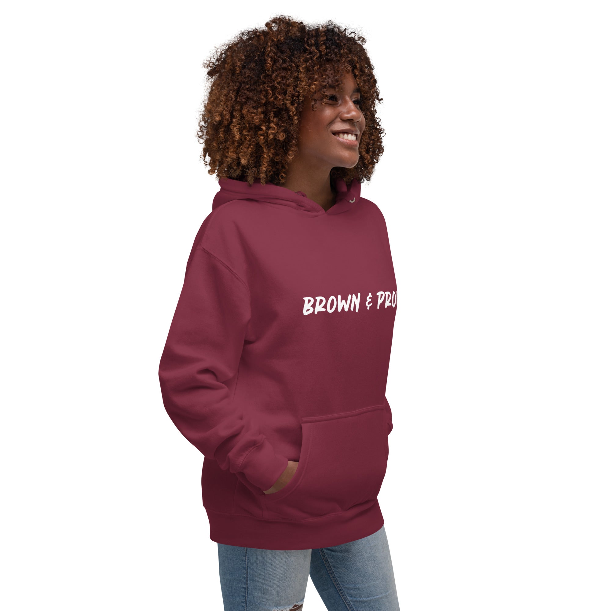 A radiant smile shines on a Black woman's face as she wears a charcoal hoodie proclaiming "Brown & Proud," capturing a moment of self-love and acceptance.