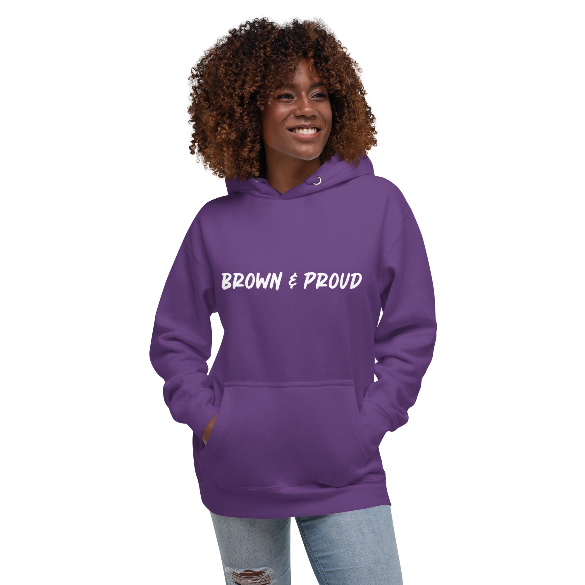 A radiant smile shines on a Black woman's face as she wears a purple hoodie proclaiming "Brown & Proud," capturing a moment of self-love and acceptance.