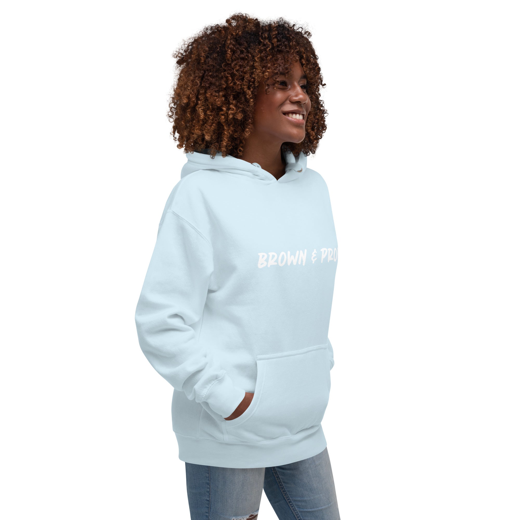 A Black woman radiates confidence, wearing a sky blue hoodie with the empowering message "Brown & Proud."