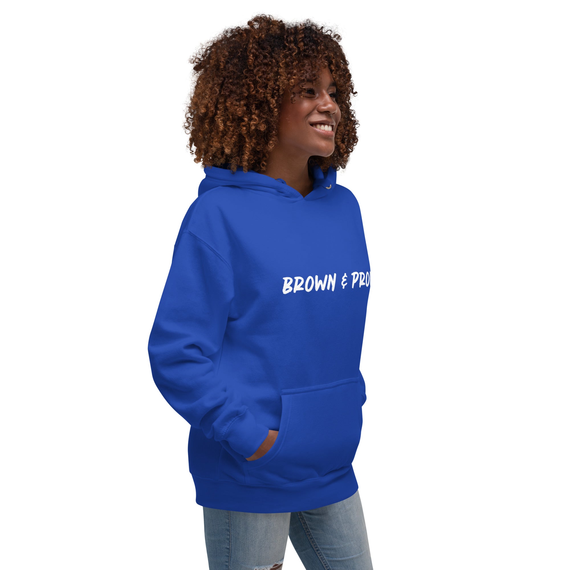 A radiant smile shines on a Black woman's face as she wears a purple hoodie proclaiming "Brown & Proud," capturing a moment of self-love and acceptance.